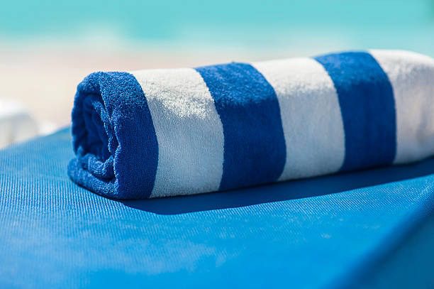 Rolled blue and white striped pool towel on a sun lounger with a blurred beach background