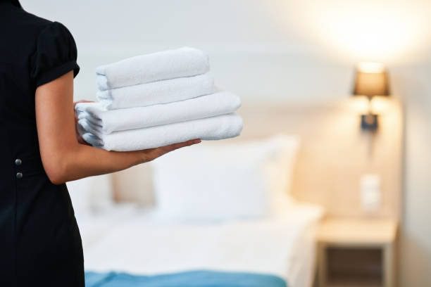Pristine white hotel bed with neatly folded towels and plush cream pillows